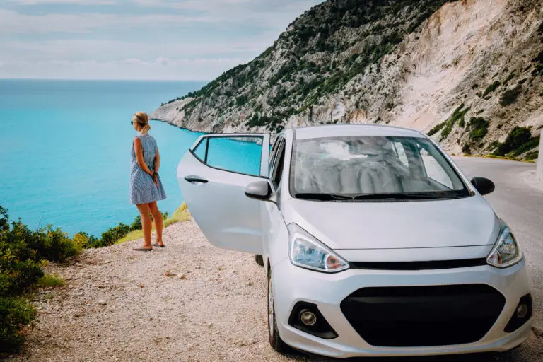 Women near rented car with open door enjoying Myrtos Beach. Travel vocation concept. Kefalonia, Ionian Sea, Greece